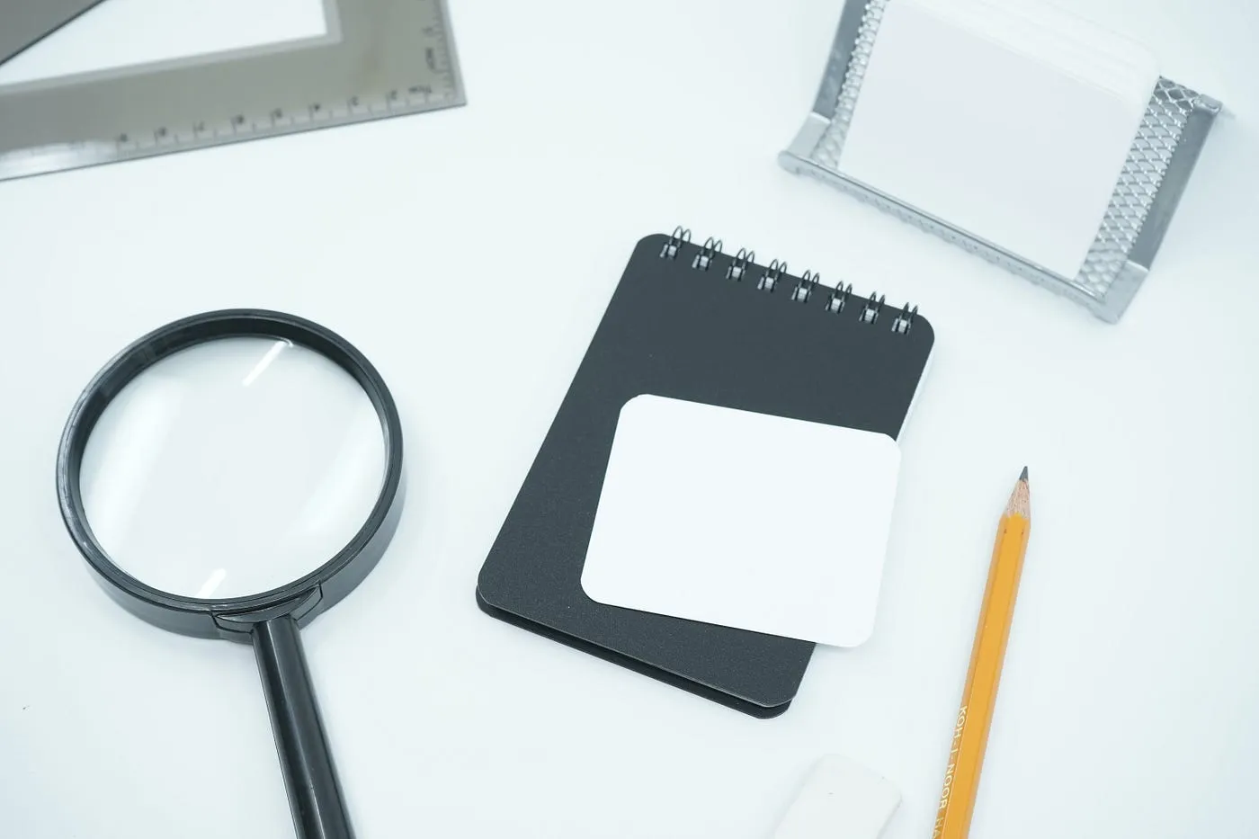 Magnifying glass, a small notebook and a pencil on a white desk