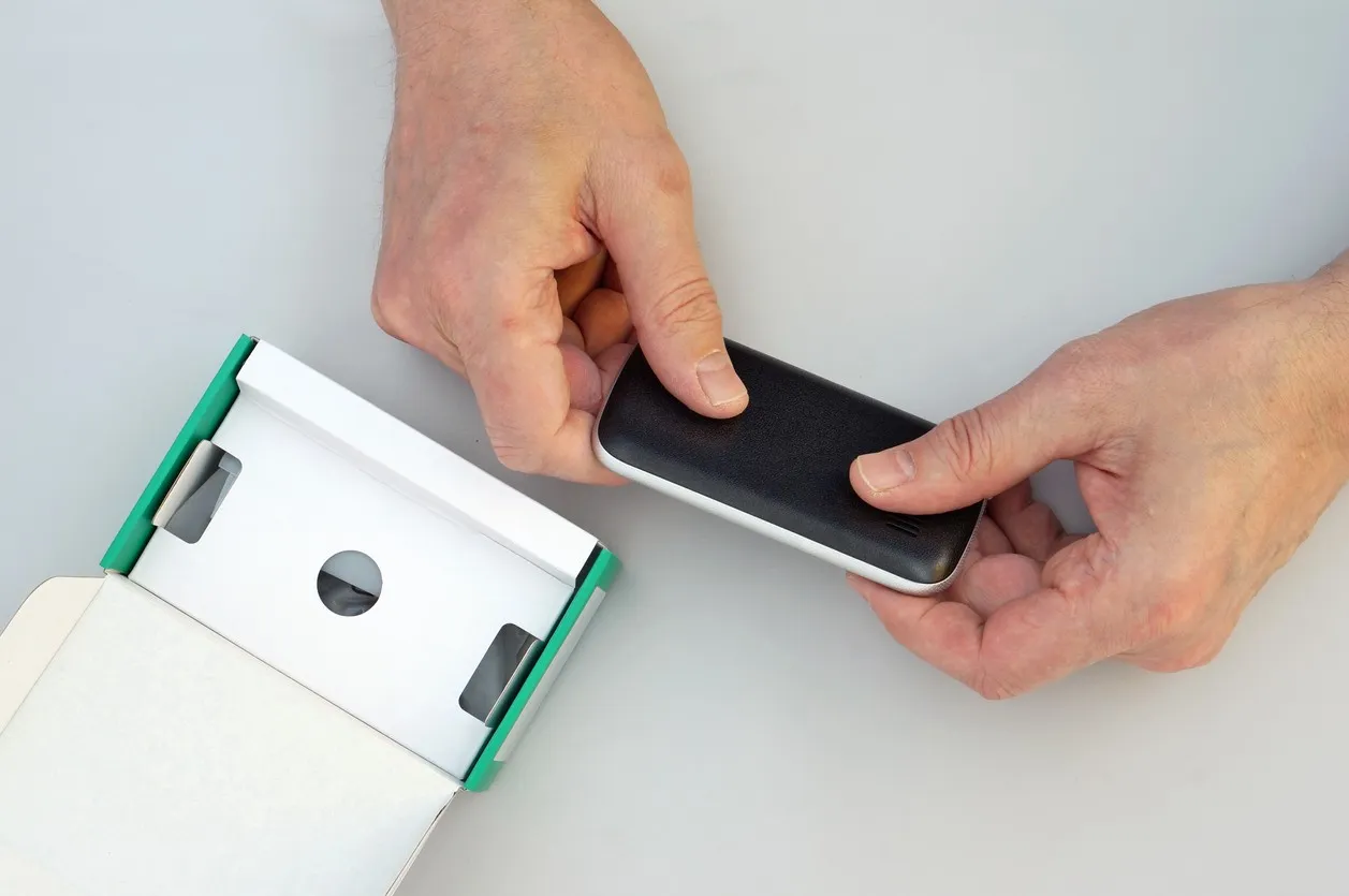 Hands lifting a small black device out of its box